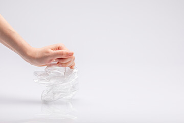 Close-up of a white people's hand crushing a crumpled plastic bottle in front of a white background