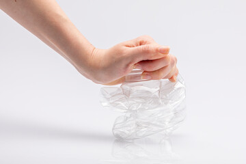 Close-up of a white people's hand crushing a crumpled plastic bottle in front of a white background