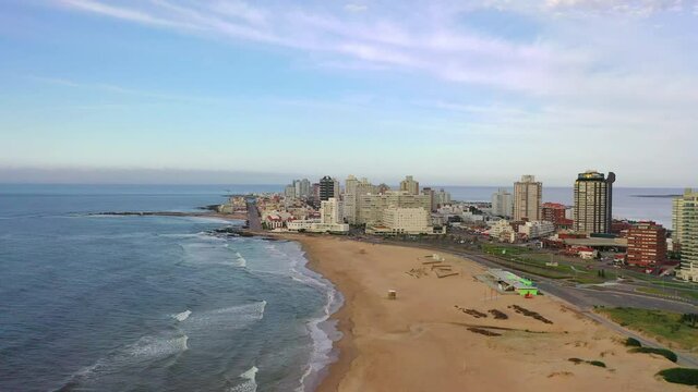 Aerial shot of beach near buildings in city against sky, drone flying forward over coastline - Punta del Este, Uruguay