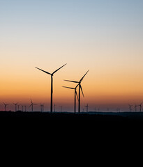 Fototapeta premium Black Silhouette of windturbines energy generator on amazing sunset at a wind farm in germany