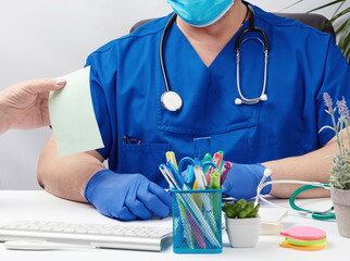 doctor in blue uniform and latex gloves sits at a white table and leads a patient reception
