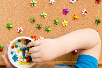 Fotobehang Flower meadow. Kids making flowers from wooden buttons and push pins on cork pin board. Therapeutic exercise for fine motoric skills and concentration of attention. © Birute