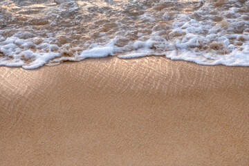 Shiny tropical sea wave with bubble on brown beach at sunset
