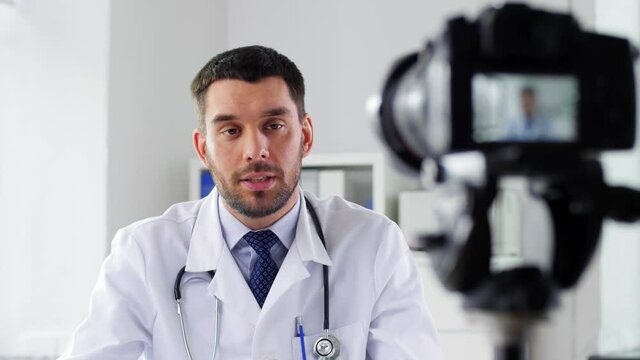 healthcare, medicine and blogging concept - male doctor with camera recording video blog at hospital