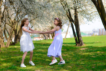 Naklejka premium Beautiful young girls with blue eyes in a white dresses in the garden with apple trees blosoming having fun and enjoying smell of flowering spring garden.