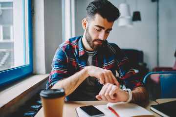 Cheerful hipster guy dressed in casual wear managing time on wristwatch - Powered by Adobe