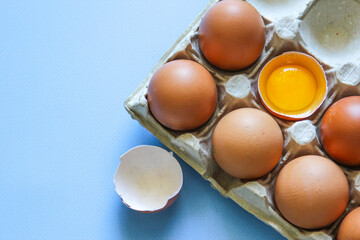 Chicken egg is half broken among other eggs. Brown eggs and egg yolk on the blue background. Top view. Flat lay.