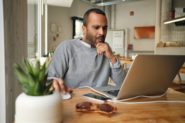 Casual businessman intently working on laptop in cafe. Thoughtful man working indoor