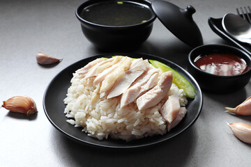 Hainanese chicken rice steam with chicken fat and garlic served in the black dish with a chicken soup on the grey table
