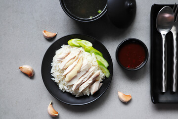 Hainanese chicken rice steam with chicken fat and garlic served in the black dish with a chicken soup on the grey table