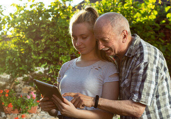 Happy granddaughter and grandfather using digital tablet outdoors