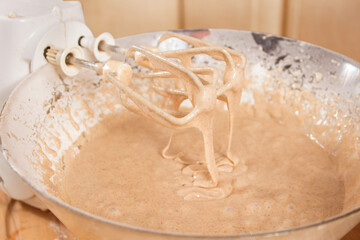 Łopatki miksera oparte o misę z rozrobionym ciastem. Z łopatek miksera spływa rozrobione ciasto.