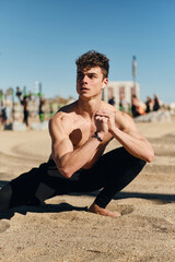 Fototapeta na wymiar Young sporty man intently stretching on beach. Handsome fit guy on functional training outdoor