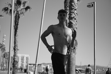 Fototapeta na wymiar Young attractive sporty man with naked torso jogging in the morning along beach. Black and white photo