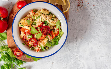 Couscous salad and grilled vegetables in the bowl, cilantro, lemon and tomatoes on a gray concrete background top view, free space for text. Vegan food. Arab or Middle Eastern cuisine.