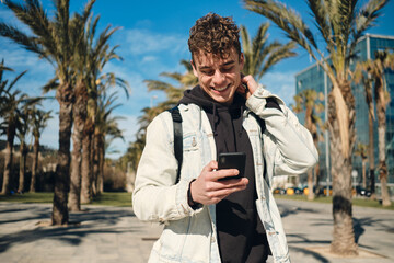 Handsome cheerful guy happily using smartphone during walk along streets. Face expression