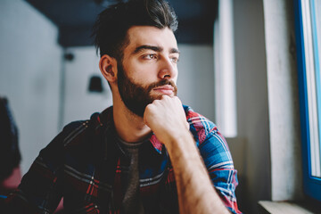 Portrait of concentrated handsome hipster guy 20 years old sitting indoors and looking in camera after course work