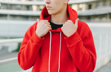 Close photo of a man in a red hoodie standing on the street and posing for the camera. Man shows...