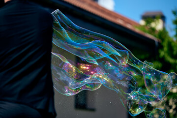 animator launches long soap bubbles at a children's holiday. shape with stick. Nature, greens and sunny day.