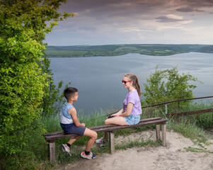 Fototapeta premium Sister and brother sitting on bench at pond
