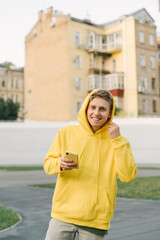 Portrait of a happy young man in a yellow hoodie stands on the background of the town landscape,...
