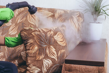 House cleaning. A girl in green gloves cleans the sofa and furniture with a steam generator. we...