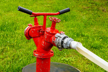 portable fire hydrant of red color with a hose on a background of green grass