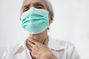 Naklejka premium Hands touching neck,sick senior female wearing protective face mask,old people has sore throat,cough,hoarseness,swelling,elderly woman suffering from throat problems,tonsillitis,painful swallowing