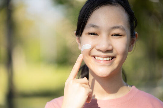 Happy Smiling Asian Child Girl Apply Sunscreen Lotion On The Cheek,protect Her Face,schoolgirl Using Skin Care Product For Sensitive Skin,sun Block Day Cream On Her Delicate Facial Skin In Sunny Day.