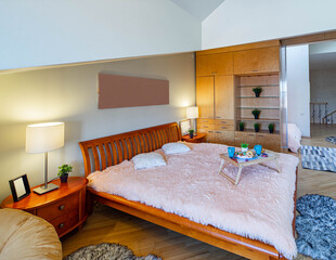 Modern interior of bedroom with wooden furniture. Tray with breakfast on the bed. Stairs. Roof windows.