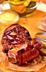 Close-up of roasted smoked pork knuckle with mustard, pickles and goat horns pepper vegetable