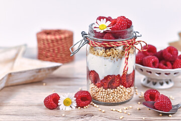 Raspberry fruit dessert with skyr yogurt, granola and puffed quinoa grains layered in jar surrounded by ingredients