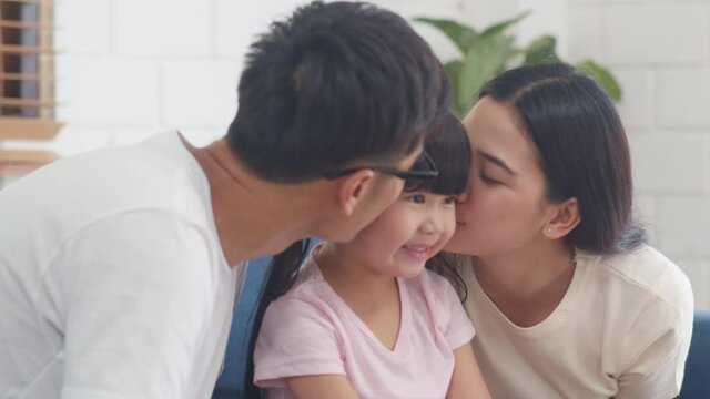 Happy Asian family dad, mom and daughter embracing kissing on cheek congratulating with birthday at house. Self-isolation, stay at home, social distancing, quarantine for coronavirus prevention.