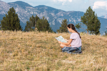 Naklejka na ściany i meble Hiker girl looking at a map sitting on the meadow in a beautiful place