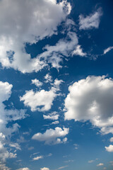 Bright white cumulus clouds in the clear blue sky on a sunny day. Vertical orientation.
