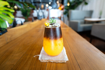 Ice black coffee mixed with orange juice placed on wooden table counter, with bistro cafe interior...
