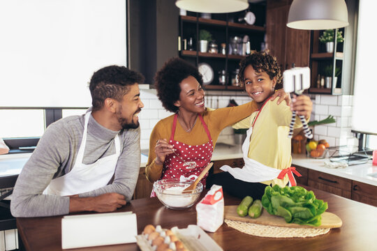 Happy black family spending day at kitchen. Girl using phone.