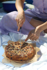 Unrecognizable person cutting sponge cake with berries and nuts, on a picnic. Selective focus.