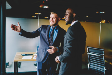 Cheerful caucasian male broker showing office interior African American entrepreneur dressed in...