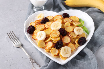 Trendy tiny pancakes with blackberry and banana in plate heart-shaped on light gray background, Space for text, Closeup