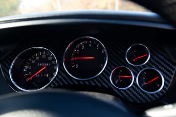 Stylish backlit dashboard with sensors for measuring speed, engine temperature and pressure against a blue and black chess designer’s design drawing in the car’s interior.