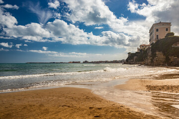 The houses and palaces of the city of Nettuno, on the cliff overlooking the sea. Cloudy blue sky, the wind, the waves of the rough sea. The Roman coast, Lazio, Italy.