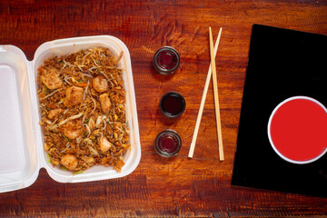Delivery Style Food in a Thermal Container with Rice, Fried Shrimps and Vegetables Served with Three Plastic Soy Sauce Containers, the Menu and Sticks