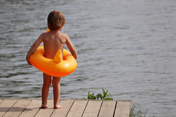 Child with a swimming circle standing on a wooden pier of summer beach. Baby boy going to swim, safety on a water