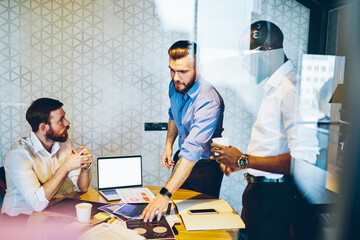 Obraz premium Multiethnic business men discussing working process in office with laptop on table