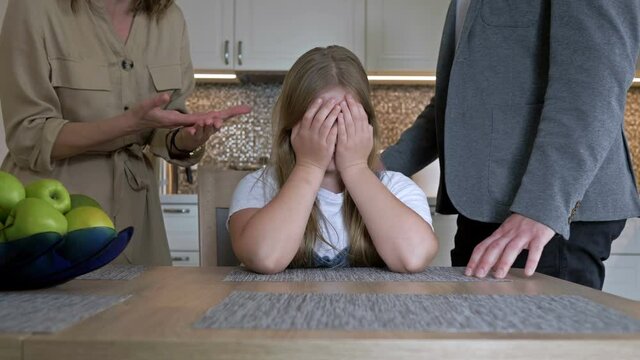 Problems of parenting in the family. Parents very much scolding a teenage daughter for something. They scream at the child. The girl helplessly covered her face with her hands.