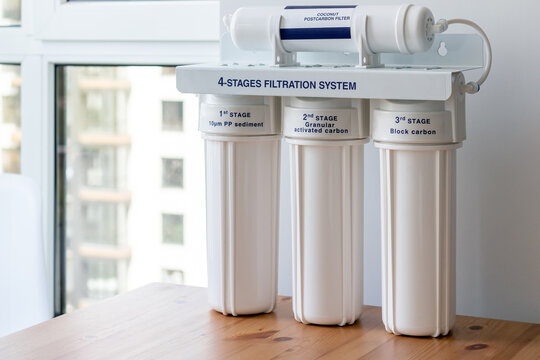 Four stages water filtration system for the home with: coconut postcarbon filter, granular activated and block carbon on a wooden table against a blurred window background. Reverse osmosis system