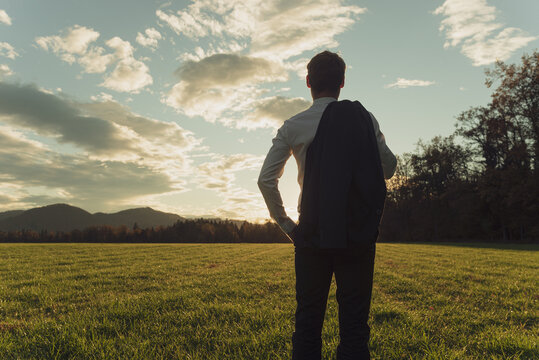 Young businessman standing in autumn meadow gazing into the future