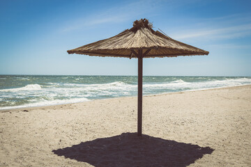 Empty beach with no people, just one eco straw wooden umbrella parasol, beautiful sea coast resort during isolation lockdown