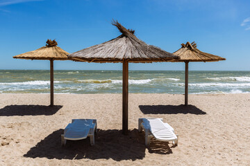 White plastic chaise longues and eco straw and wooden umbrellas parasol at empty beach, ukrainian resort Berdyansk during isolation lockdown quarantine, beautiful Azov sea coast with nobody